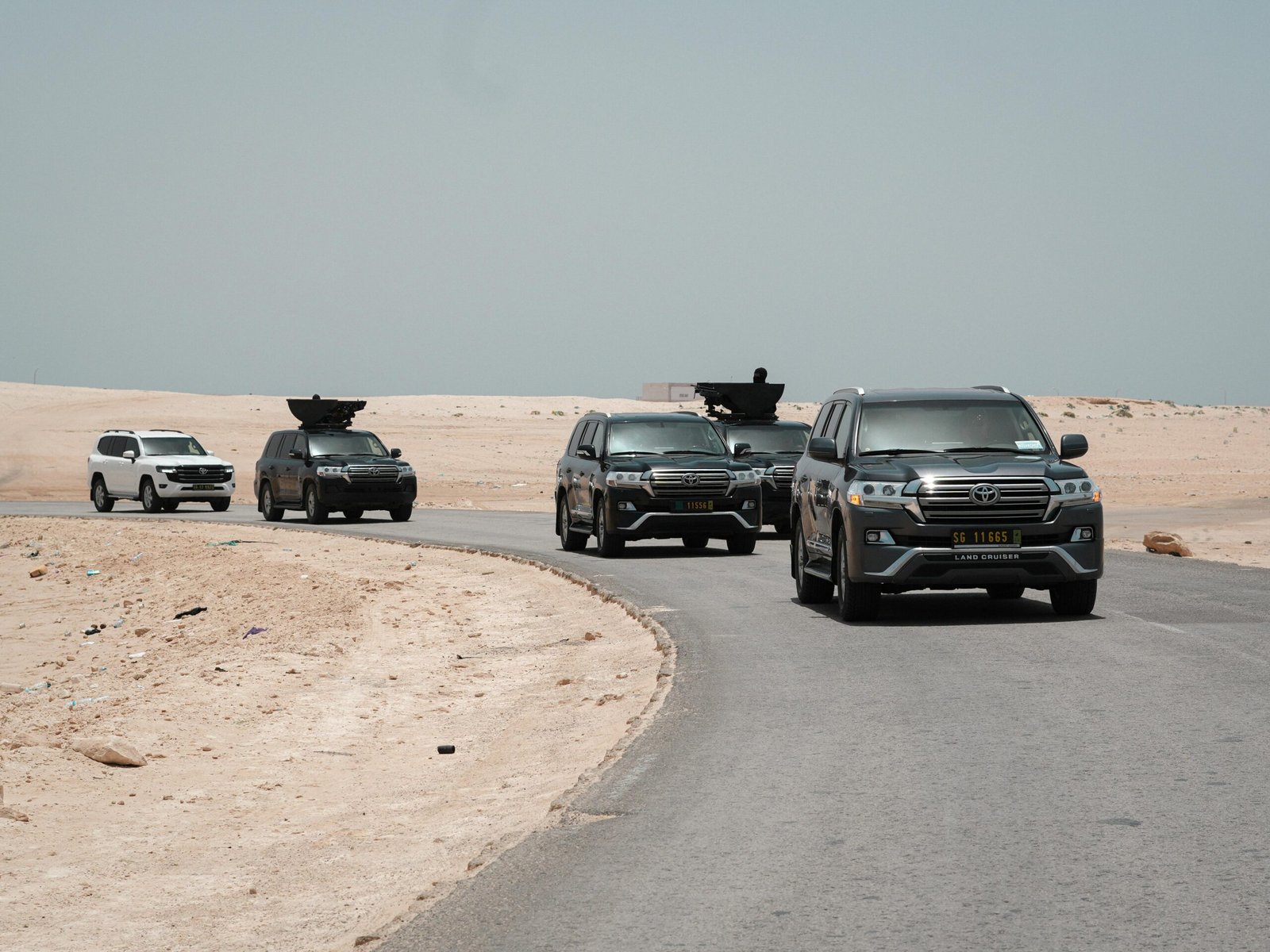 A convoy of armored SUVs traversing a deserted desert road under a clear sky.