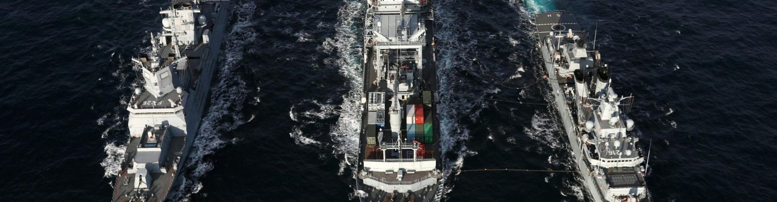 Naval ships sailing in formation on open sea, aerial view highlights naval coordination and strategy.